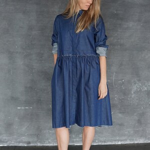 May include: A woman wearing a blue denim shirt dress with a black hat and black ankle boots.