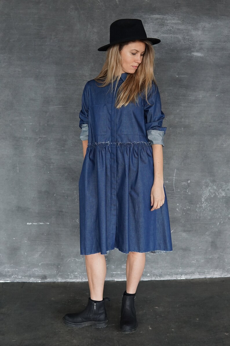May include: A woman wearing a blue denim shirt dress with a black hat and black ankle boots.