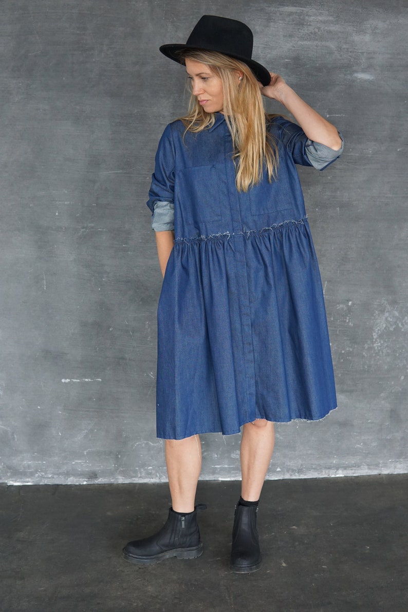 May include: A woman wearing a blue denim shirt dress with a black hat and black ankle boots.