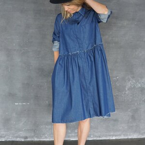May include: A woman wearing a blue denim shirt dress with a black hat and black ankle boots.