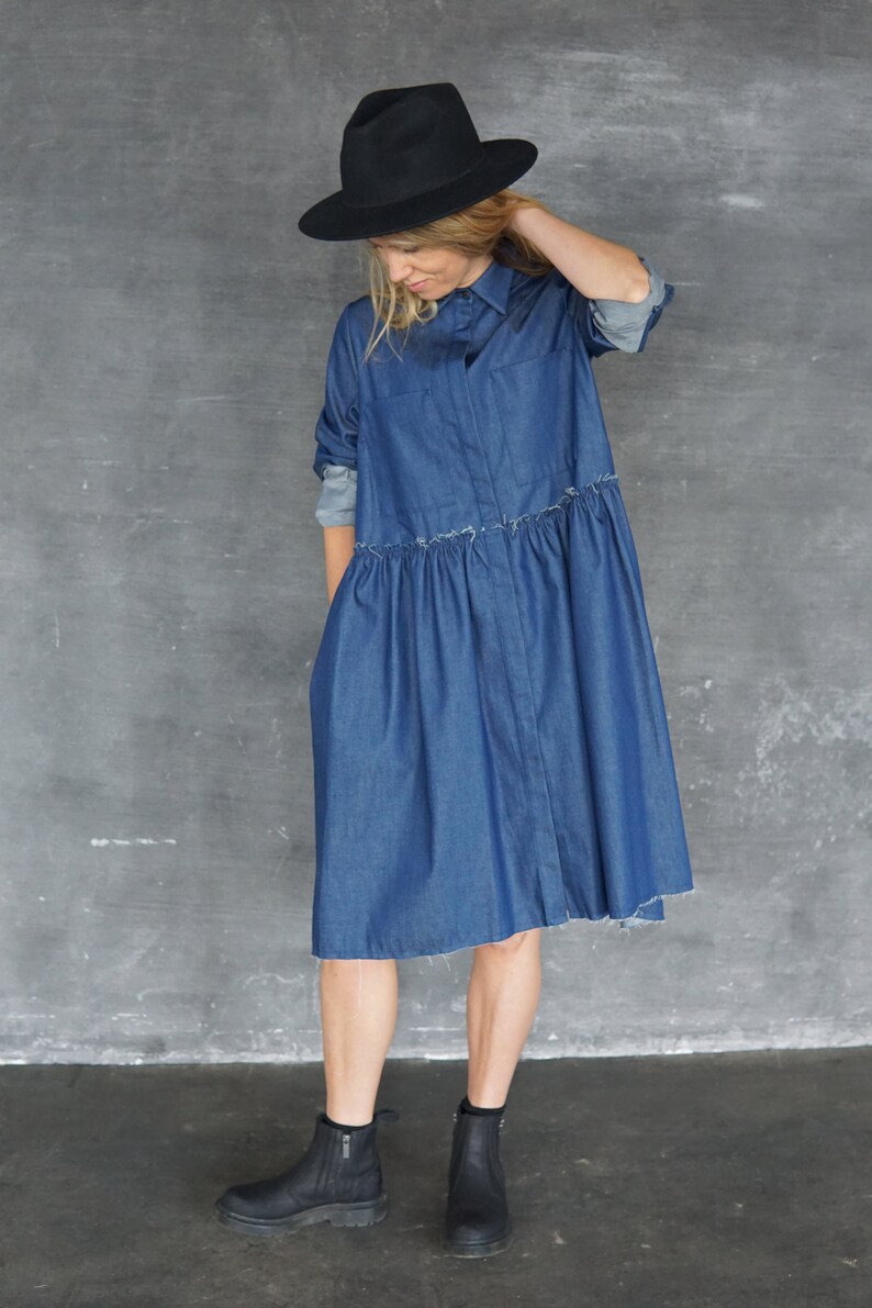 May include: A woman wearing a blue denim shirt dress with a black hat and black ankle boots.