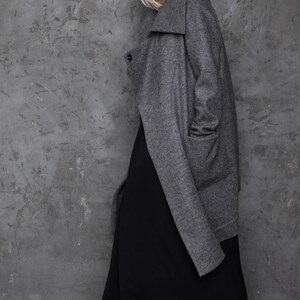 Pu&ograve; includere: Un cappotto grigio a maniche lunghe con un ampio colletto e una gonna maxi nera. Il cappotto ha una chiusura con un solo bottone e una tasca sul lato sinistro.