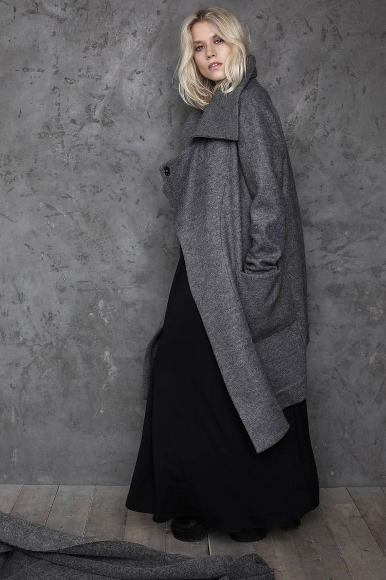 Pu&ograve; includere: Un cappotto grigio a maniche lunghe con un ampio colletto e una gonna maxi nera. Il cappotto ha una chiusura con un solo bottone e una tasca sul lato sinistro.