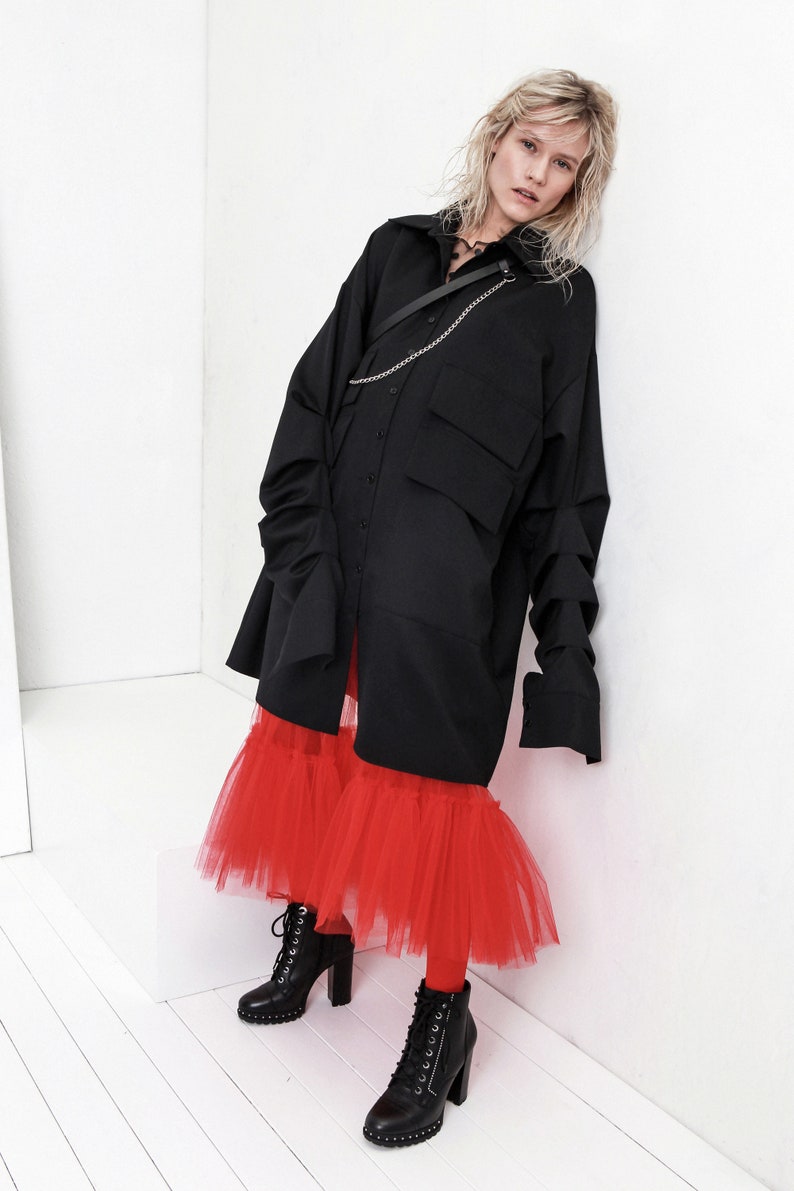 Op de afbeelding: Een zwart oversized shirt met een kettingdetail gedragen over een rode tule rok en zwarte laarzen met hak.