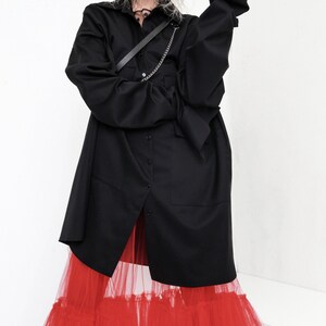 Op de afbeelding: Een zwart oversized shirt met lange mouw en een rode tule rok met meerdere lagen.