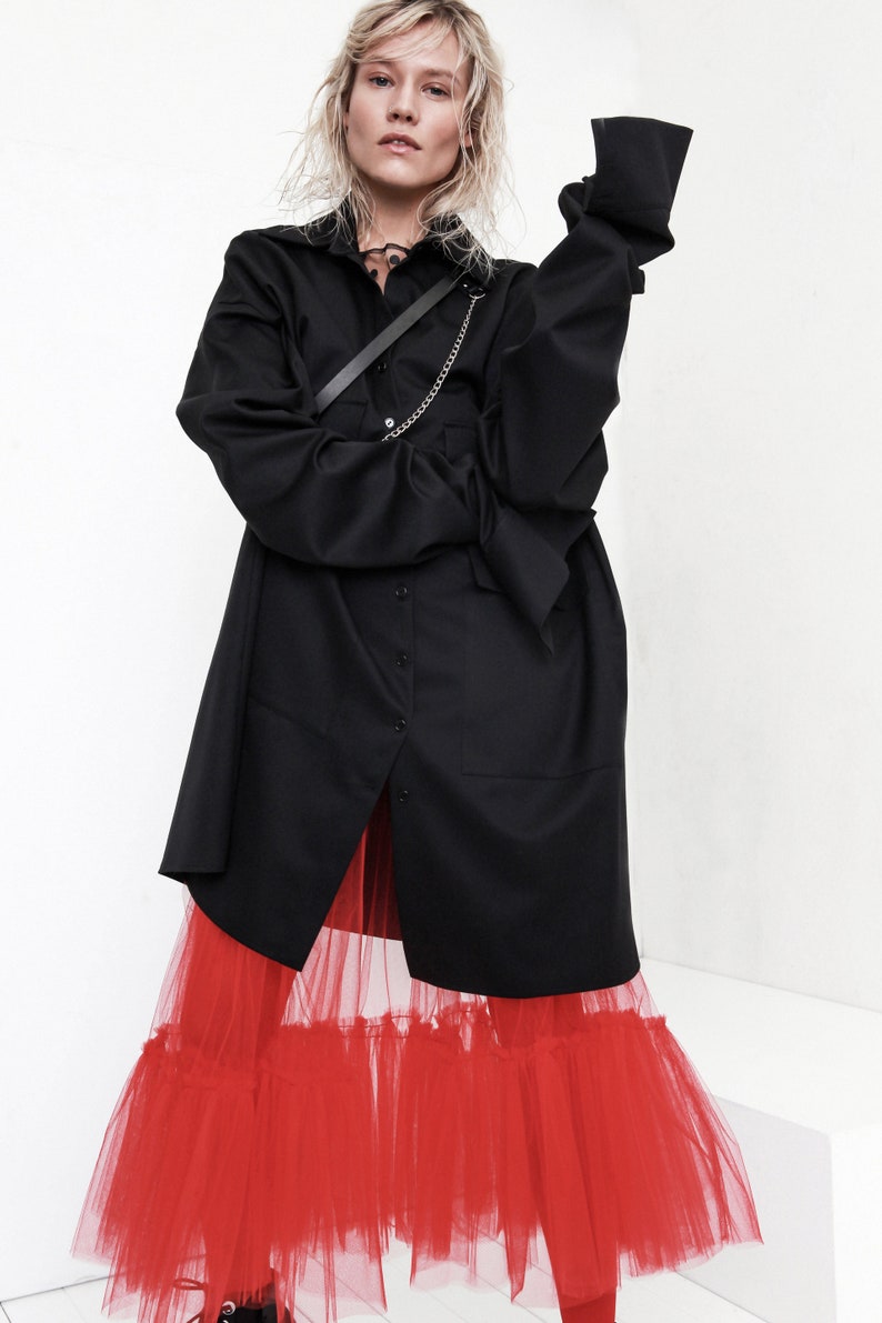 Op de afbeelding: Een zwart oversized shirt met lange mouw en een rode tule rok met meerdere lagen.