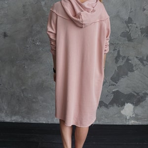 May include: A long, dusty rose hooded sweatshirt dress with a relaxed fit and a slightly frayed hem.