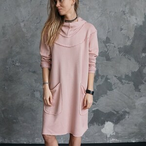 May include: A pink, long-sleeved, hooded dress with two pockets and a frayed hem.