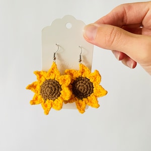 Op de afbeelding: Een paar gehaakte zonnebloem oorbellen met bruine centra en gele bloemblaadjes. De oorbellen hangen aan zilveren haakjes.