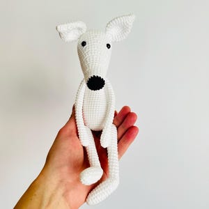 May include: White crocheted dog toy with black eyes and nose. The toy is sitting in a person's hand.