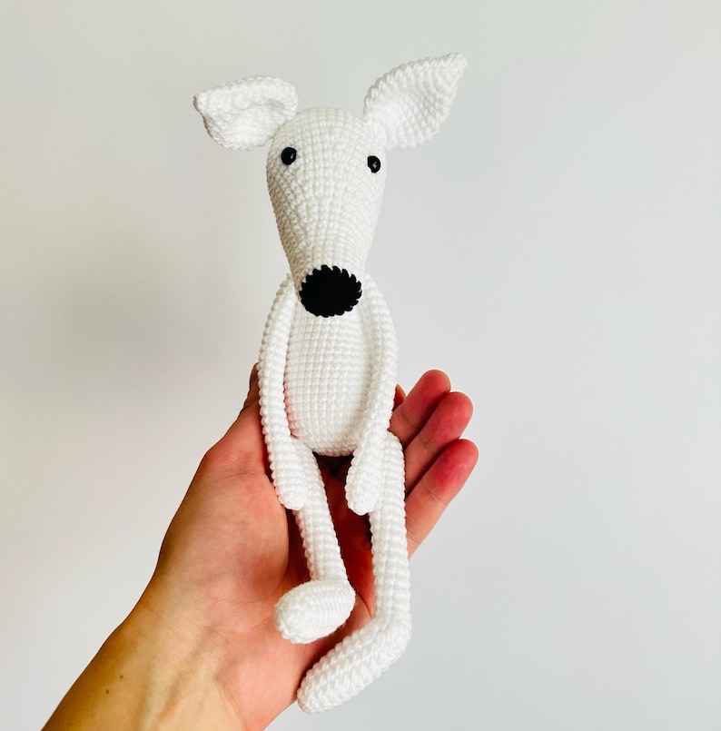 May include: White crocheted dog toy with black eyes and nose. The toy is sitting in a person's hand.