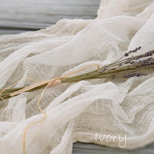 May include: A small bundle of dried purple lavender stems tied with a thin tan twine, resting on a piece of crinkled, semi-sheer ivory fabric. The word ivory is printed in white text at the bottom right corner of the image.
