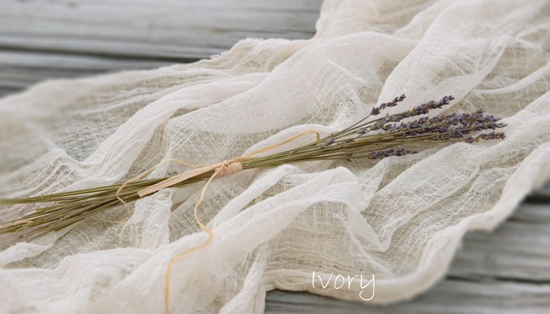 May include: A small bundle of dried purple lavender stems tied with a thin tan twine, resting on a piece of crinkled, semi-sheer ivory fabric. The word ivory is printed in white text at the bottom right corner of the image.