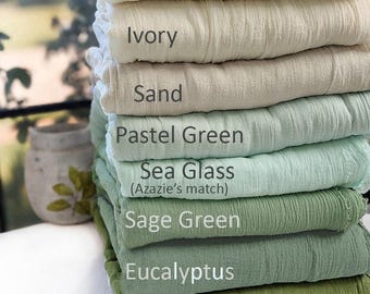 May include: A stack of folded fabric swatches in various shades of green and neutral tones. The colors are labeled as Cream, Ivory, Sand, Pastel Green, Sea Glass (Azazie's match), Sage Green, Eucalyptus, and Cocktail Olive with a crinkled texture.