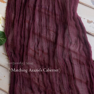 May include: Burgundy or wine colored sheer fabric with a crinkled texture. The fabric is draped over a white wooden surface. The text "Matching Azazie's Cabernet" is written on the fabric.