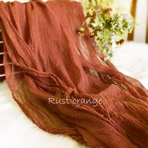 May include: A rust orange fabric backdrop with a textured, crinkled look. The fabric is draped over a white metal chair and has a soft, flowing appearance.