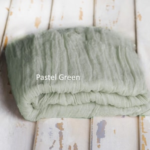 May include: A folded piece of pastel green fabric with a crinkled, textured surface. The textile features a loose, gauze-like weave and is labeled with the text Pastel Green printed directly onto the center of the fabric surface.