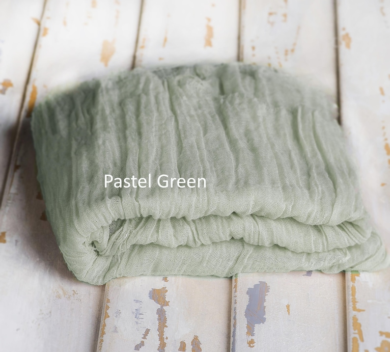 May include: A folded piece of pastel green fabric with a crinkled, textured surface. The textile features a loose, gauze-like weave and is labeled with the text Pastel Green printed directly onto the center of the fabric surface.
