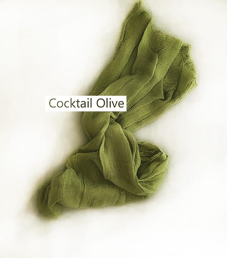 May include: A long, rectangular piece of olive green fabric with a crinkled, textured surface. The fabric is draped in a loose, flowing manner. A white rectangular label with the black text Cocktail Olive is positioned over the fabric.