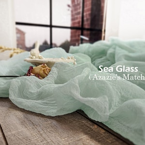 May include: Sea Glass (Azazie's Match) is written on a light green sheer fabric backdrop. The fabric is draped over a wooden surface.