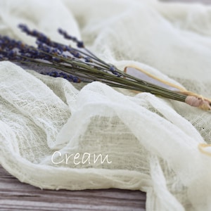 May include: A cream-colored, semi-sheer, crinkled fabric runner draped in soft folds. A small bundle of dried purple lavender stems is tied together with a thin, light-colored string and rests on top of the fabric. The word Cream is printed in white.