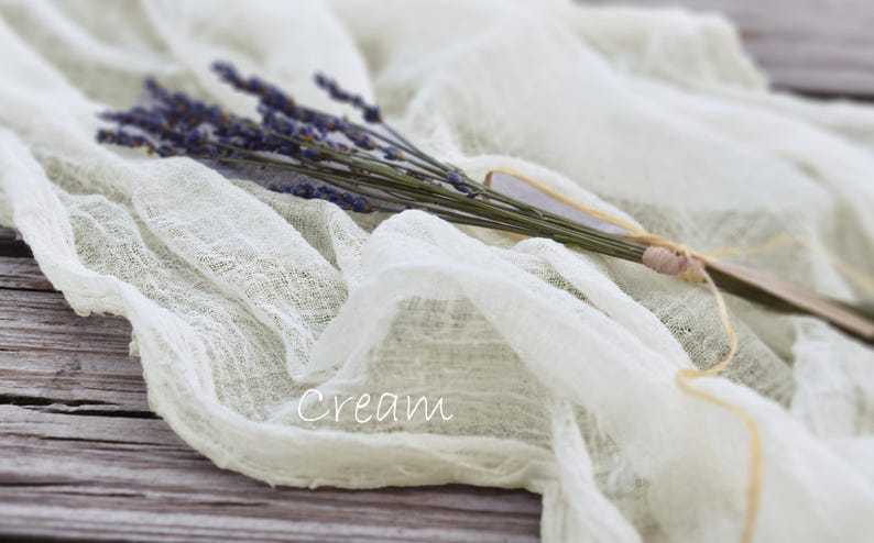 May include: A cream-colored, semi-sheer, crinkled fabric runner draped in soft folds. A small bundle of dried purple lavender stems is tied together with a thin, light-colored string and rests on top of the fabric. The word Cream is printed in white.