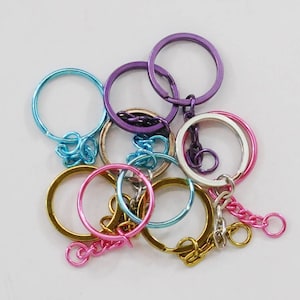 Op de afbeelding: Een set kleurrijke metalen sleutelhangers in verschillende tinten blauw, paars, roze en goud. De sleutelhangers zijn met een zilveren ketting aan elkaar verbonden.