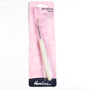 Op de afbeelding: Witte plastic vullingstool op een roze en witte verpakking. De kaart heeft de tekst "Stuffing Tool" en "Perfect voor het vullen van vullingsmaterialen in kleine gebieden, hoeken etc."