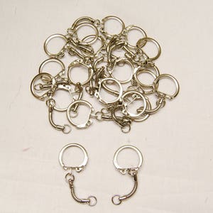May include: A pile of silver key rings with a spring-loaded clasp. Two key rings are separated from the pile and have a silver chain attached.