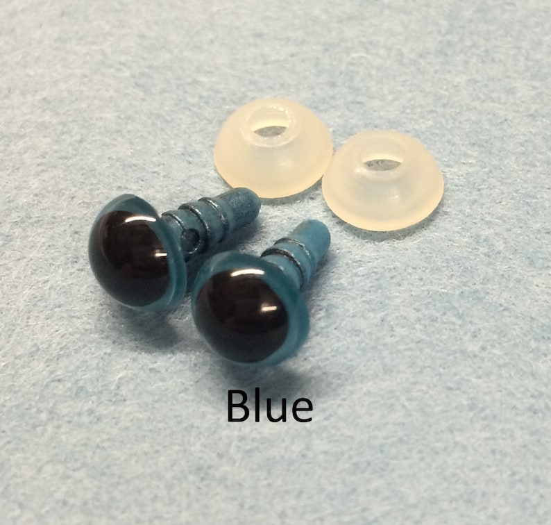 May include: Two blue plastic safety eyes with black pupils and metal shanks. The eyes are on a light blue surface with two white plastic washers.