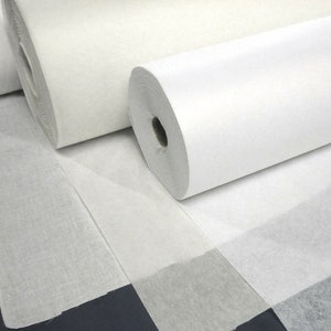 May include: Three rolls of white non-woven fabric. The fabric is rolled up and the ends are visible. The fabric is smooth and has a slight sheen.