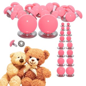 Puede incluir: Un conjunto de ojos de seguridad de pl&aacute;stico rosa para peluches, con superficies lisas, redondas y brillantes con arandelas met&aacute;licas. El set incluye varios tama&ntilde;os, con dos ojos grandes colocados sobre dos osos de peluche marrones.
