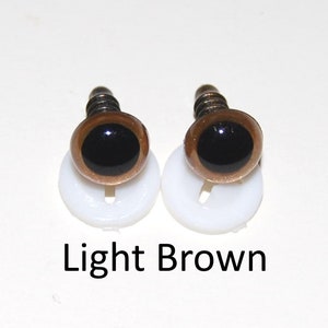 May include: Two light brown plastic safety eyes with black pupils, mounted on white plastic bases. The eyes are for craft projects.
