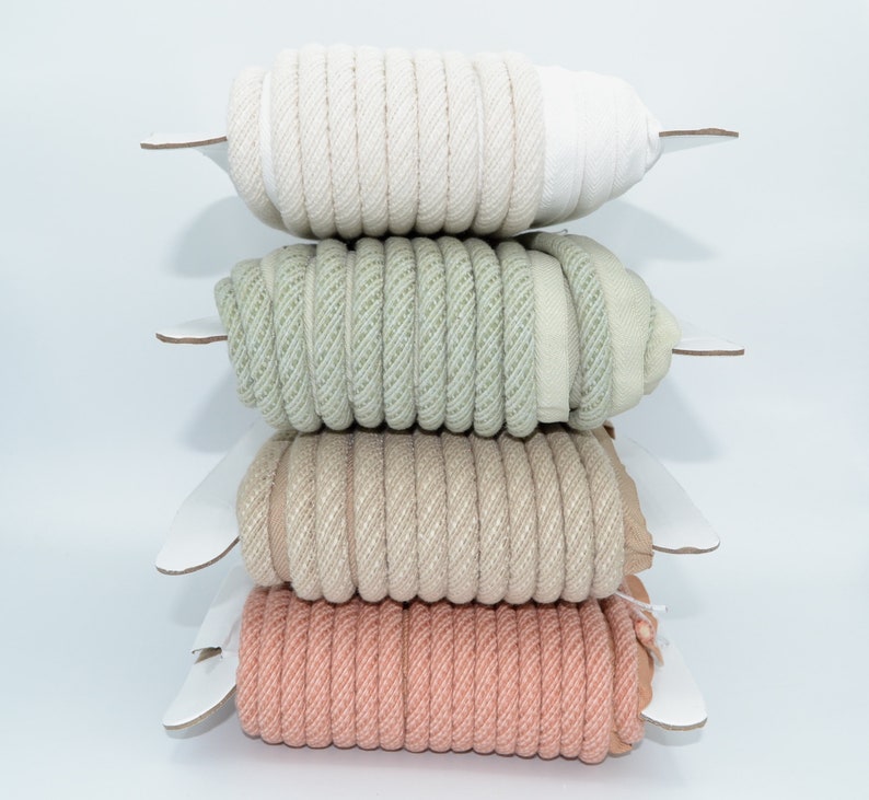 Pu&ograve; includere: Quattro bobine di corda intrecciata di diversi colori, impilate l'una sull'altra. Le bobine sono bianche, verde chiaro, beige e rosa.