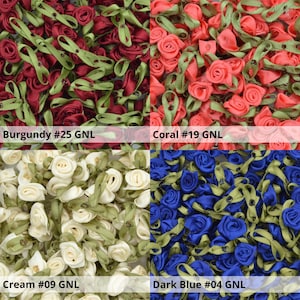 May include: Assortment of four colors of small fabric rose embellishments. Burgundy, coral, cream, and dark blue fabric roses with green stems and leaves.
