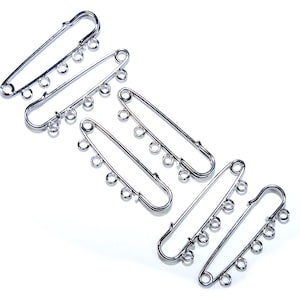 May include: Four silver safety pins with multiple loops for attaching fabric or other materials.