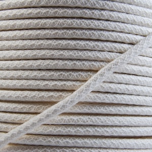 May include: A close-up of a spool of white cotton cord. The cord is tightly wound and has a textured surface.