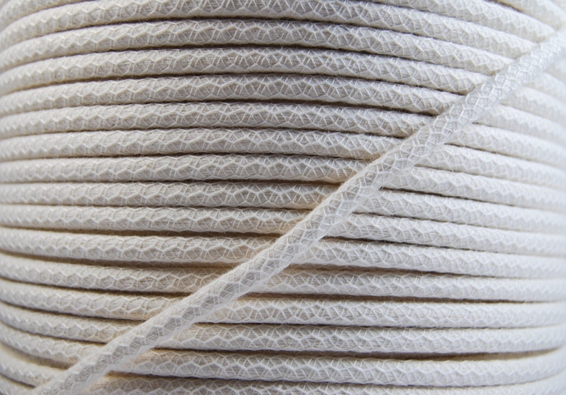 May include: A close-up of a spool of white cotton cord. The cord is tightly wound and has a textured surface.