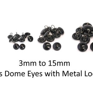 May include: A collection of black glass dome eyes with metal loops, arranged in four size groups ranging from 3mm to 15mm. The smooth, round, glossy black surfaces reflect light, and each piece features a small metal loop on the back for attachment.