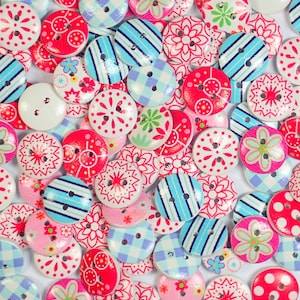 May include: Assortment of colourful wooden buttons with various patterns, including floral, geometric, and polka dots. The buttons are in shades of pink, blue, red, and white.