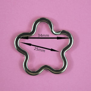 May include: Silver-toned metal flower-shaped key chain with measurements: 34mm x 25mm.