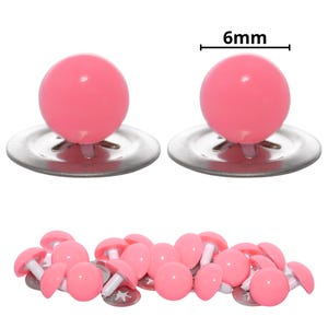 Puede incluir: Un conjunto de ojos de seguridad de pl&aacute;stico rosa para manualidades, cada uno con una cabeza rosa lisa, redonda y brillante unida a un poste de pl&aacute;stico blanco y una arandela de metal. El di&aacute;metro de cada ojo est&aacute; marcado como 6mm en la imagen.