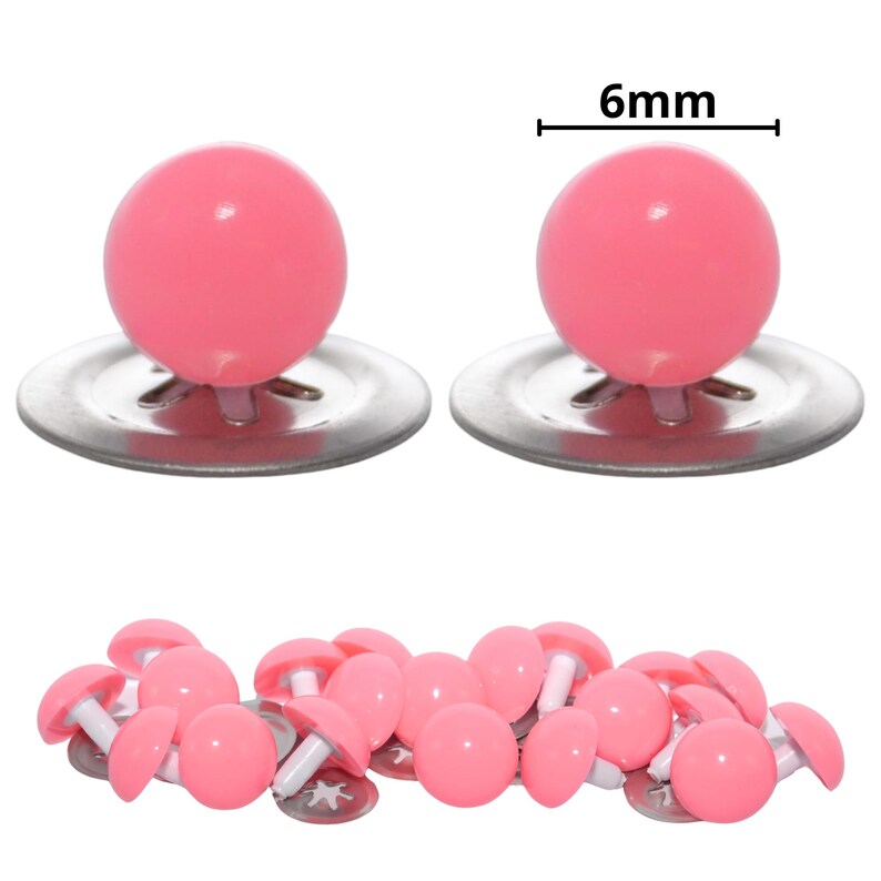 Puede incluir: Un conjunto de ojos de seguridad de pl&aacute;stico rosa para manualidades, cada uno con una cabeza rosa lisa, redonda y brillante unida a un poste de pl&aacute;stico blanco y una arandela de metal. El di&aacute;metro de cada ojo est&aacute; marcado como 6mm en la imagen.