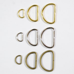 May include: Assortment of metal D-rings in three sizes and three finishes: gold, silver, and antique brass.