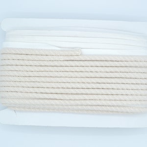 Pu&ograve; includere: Un rotolo di cordoncino di cotone di colore naturale avvolto in carta bianca. Il cordoncino &egrave; spesso e ha una texture simile a una corda.