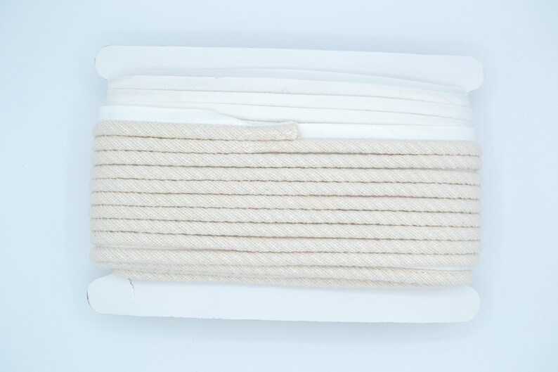 Pu&ograve; includere: Un rotolo di cordoncino di cotone di colore naturale avvolto in carta bianca. Il cordoncino &egrave; spesso e ha una texture simile a una corda.