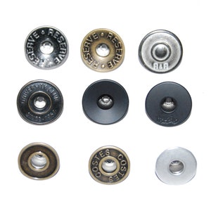 Peut inclure: Assortiment de neuf boutons métalliques de différentes couleurs et designs. Les boutons présentent différents textes, notamment "Reserve", "University Club" et "Costes".