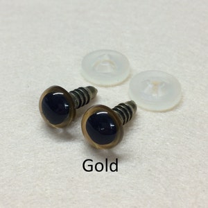 May include: Two gold plastic safety eyes with black pupils and screw backs. The eyes are on a white surface with two clear plastic washers.