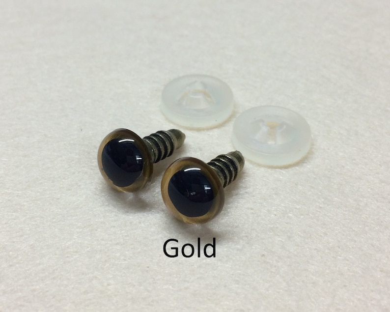 May include: Two gold plastic safety eyes with black pupils and screw backs. The eyes are on a white surface with two clear plastic washers.
