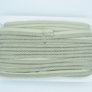 Pu&ograve; includere: Un rotolo di cordoncino intrecciato beige e bianco, perfetto per progetti di artigianato.